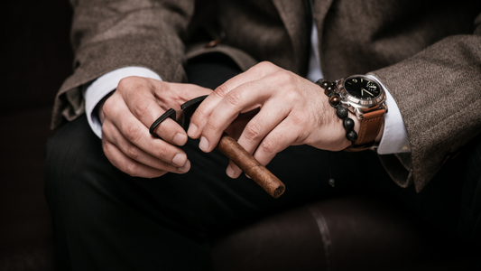 man's hands cutting a cigar with a nice watch and suit on